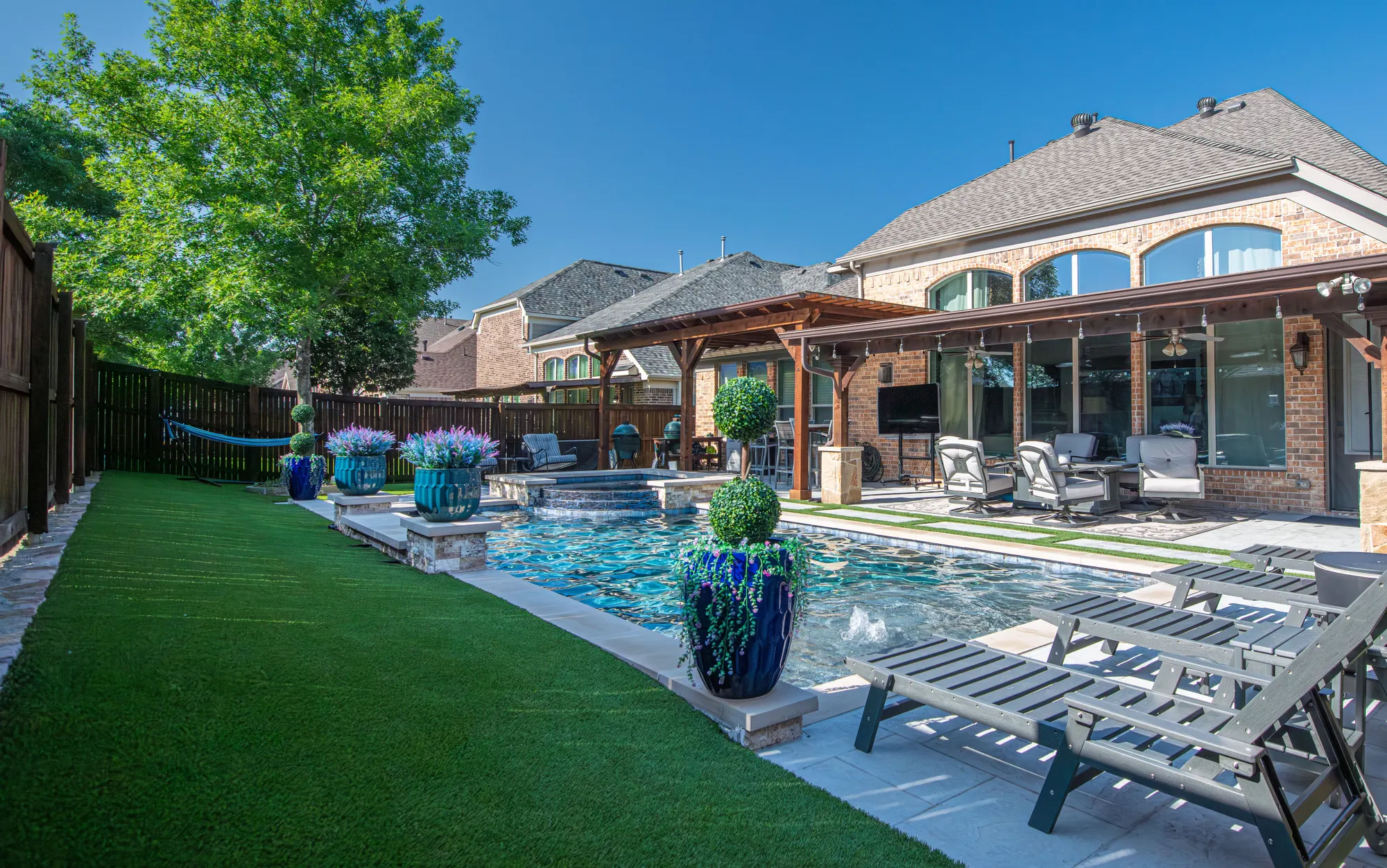 Backyard with an artificial turf lawn beside a pool and a covered patio