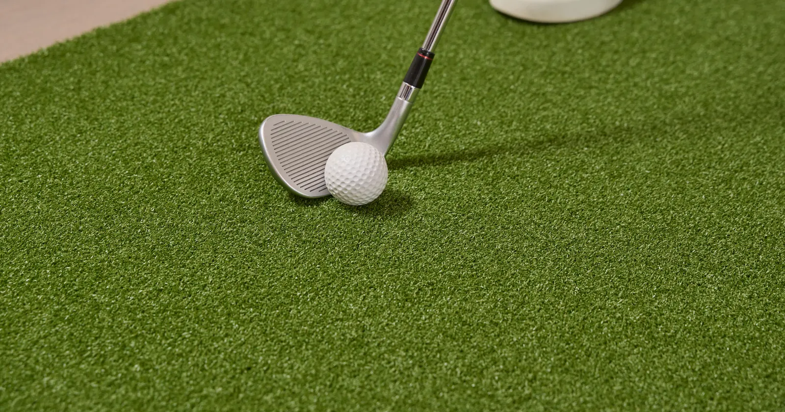 Wedge behind a golf ball on artificial turf fringe